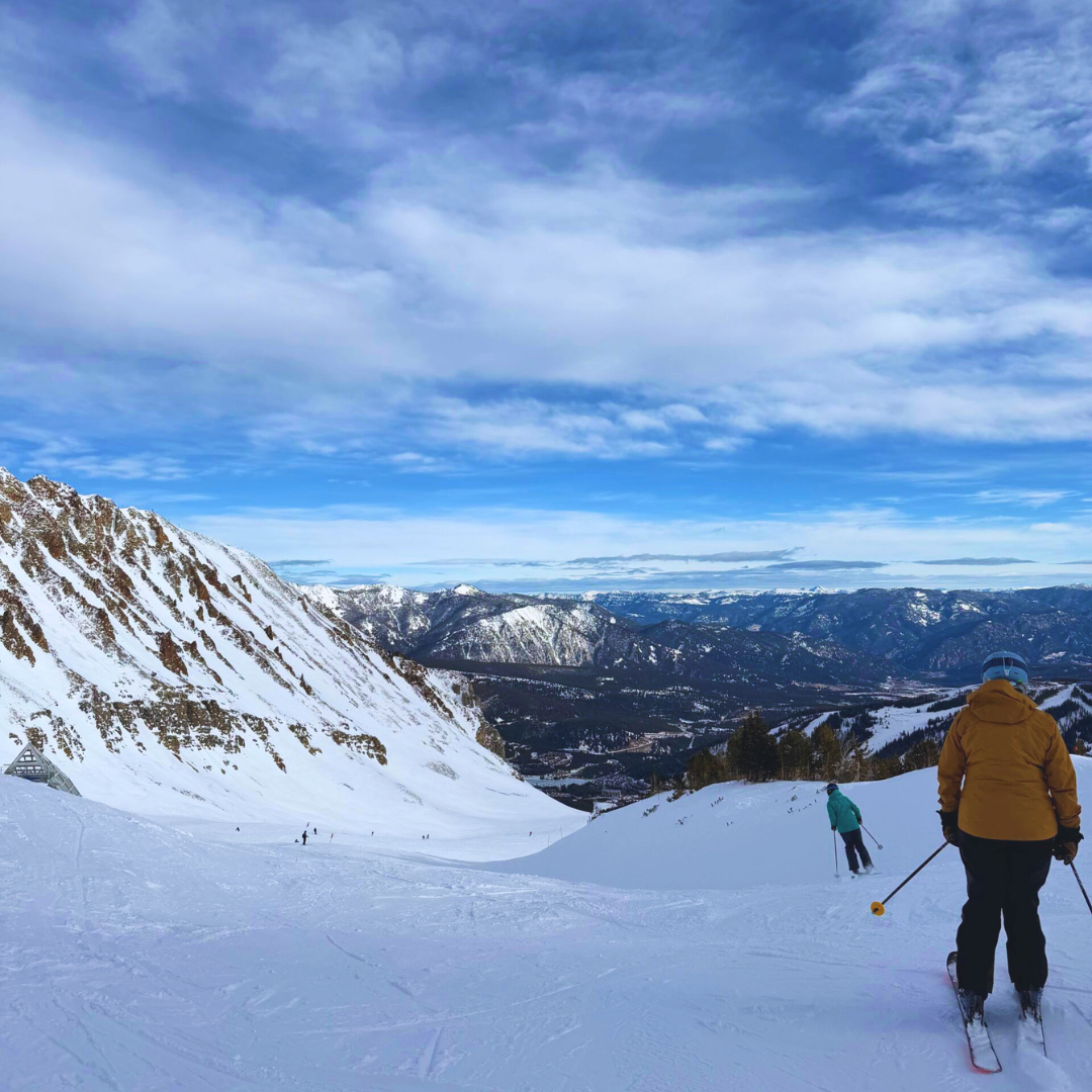 A snowy mountain ski run at sunrise with pine trees on either side and a clear blue sky above, representing the Whitefish, Montana-style destinations available through AdventureEXP seasonal placements.
